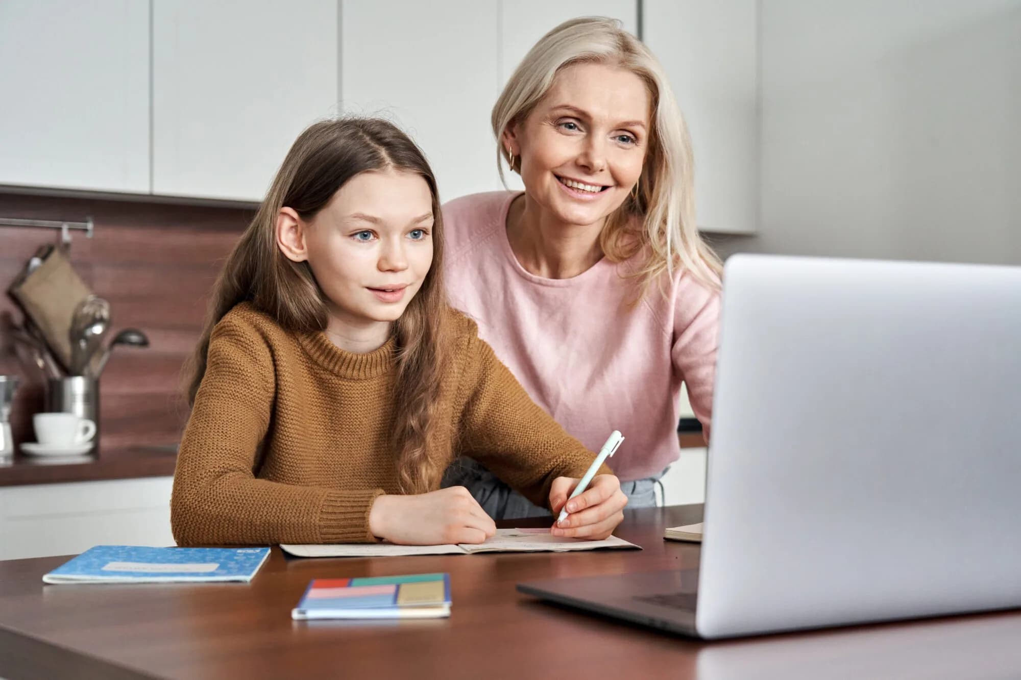 A parent and her daughter working together on a laptop at the kitchen table